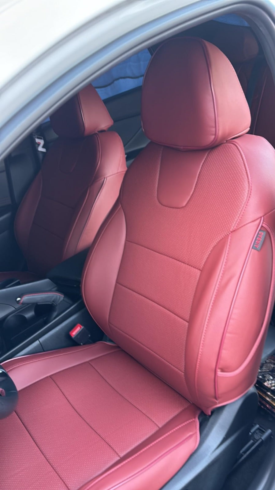 Front seats of Hyundai Tucson covered with burgundy artificial nappa leather seat covers, showing detailed stitching and Airbag tag