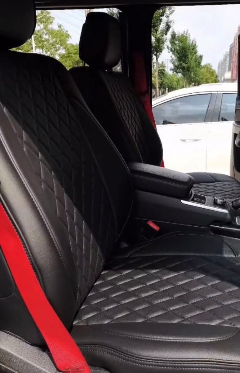 Front two seats covered in black artificial nappa leather with diamond stitching and red seat belts in a Mercedes Benz G Class
