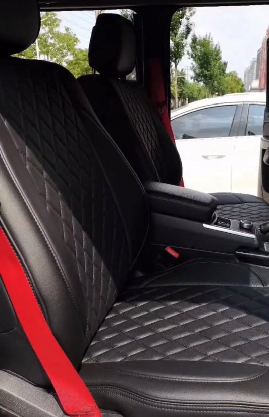 Front two seats covered in black artificial nappa leather with diamond stitching and red seat belts in a Mercedes Benz G Class